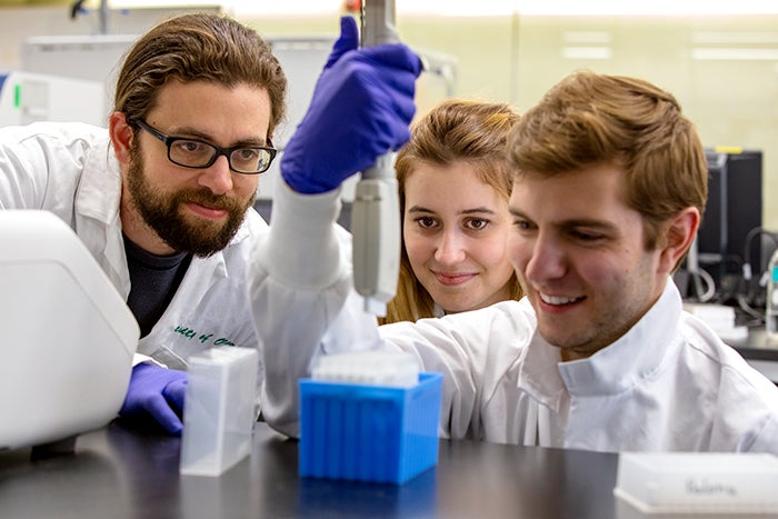 Three student researchers working and smiling in the lab.